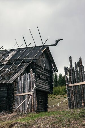 Ruins of a hedge and an old abandoned wooden house with roof decorationsの写真素材