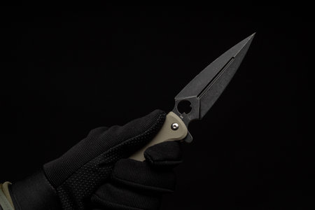 Hand in a black glove holds a pocket knife with a black bladeの写真素材