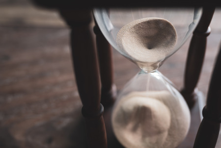 Close-up Vintage Wooden Hourglass on Wooden Background, 
Sand running through the bulbs for measuring the passing time in a countdown to a deadline.の写真素材
