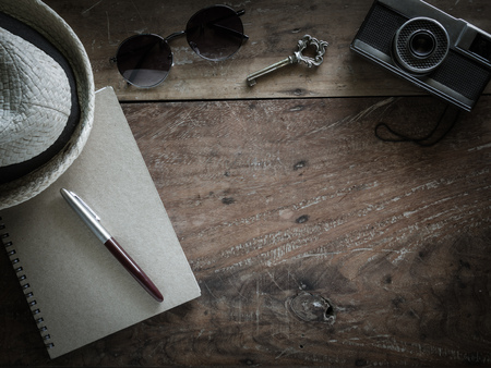 The classic silver pen on the recycle notebook cover with antique key, sunglasses, vintage camera and white weave hat on old wooden background for traveler journey conceptの写真素材