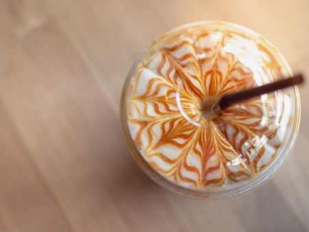 Close-up Iced Caramel Macchiato with Brown Straw in Take Home Plastic Glass on Wooden Background,...