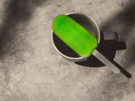 Green Ice Pop on Ceramic Glass with Light and Shadow on Cement Background in Monochrome Art Styleの写真素材