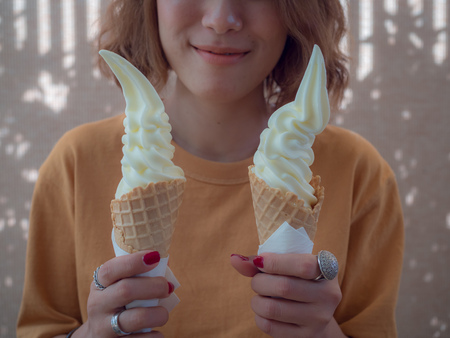 Beautiful Woman Short Hair Wearing Yellow Shirt Holding Two Soft Serve Vanilla Ice Cream Cones on Summer Timeの写真素材