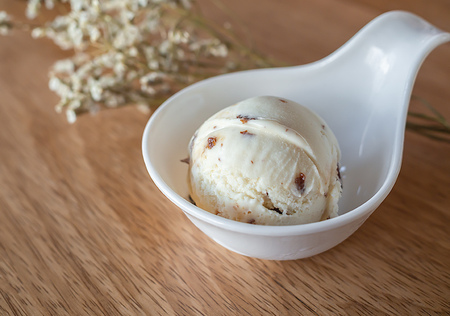 Scoop of Homemade Rum Raisin Ice Cream in Little White Cup on Wooden Backgroundの写真素材