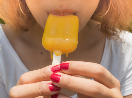 Beautiful Woman Short Hair Wearing White Shirt Eating Yellow Ice Pop Melting on Her Hand on Summer Timeの写真素材