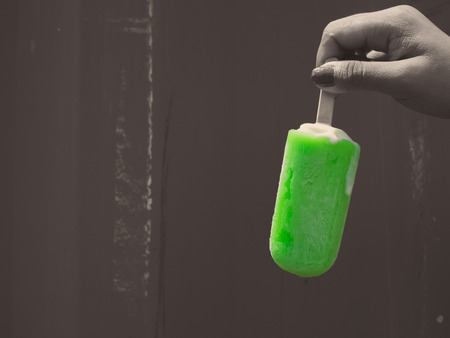 Womanâs Hand Holding Green Frozen Ice Pop Upside Down on Grunge Wall Background in Monochrome Art Styleの写真素材