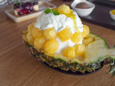 Ice Cream Snow Flake. Sweet Dessert Korean Style call Bingsu with Pineapple Flavor Ice Ball in A Bowl Made by A Half of Fresh Pineapple on Wooden Table Cafe Backgroundの写真素材