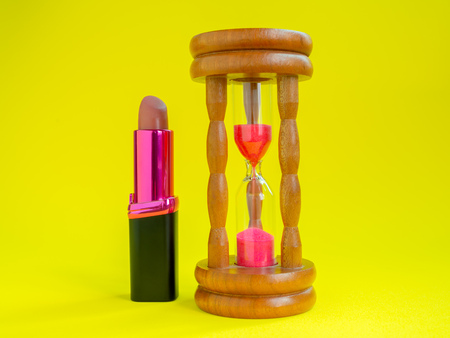 Time and Cosmetic, Vintage Hourglass and Lipstick on Yellow Background. Beauty Rejuvenation Concept.の写真素材