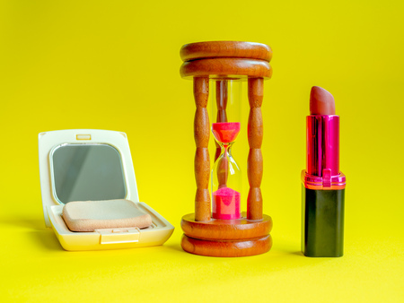 Time and Cosmetic, Vintage Hourglass, Lipstick and Face Powder Puff on Yellow Background. Beauty Rejuvenation Concept.の写真素材