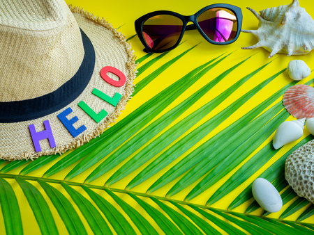 Flat Lay Beach Accessories, Beach Hat, Colorful Seed Bead Necklace, Sunglasses with Hello Colourful Text, Beach Seashells, Coral, Beach Pebbles and Coconut Palm Leaf on Lemon Yellow Background. Top View Vacation Summer Concept.の写真素材