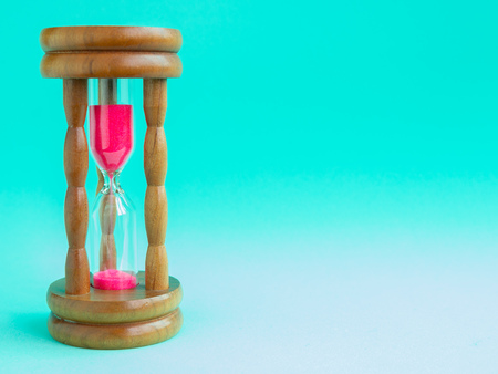 Wooden Vintage Hourglass with Pink Sand on Blue Background, Sand Running through the Bulbs for Measuring The Passing Time in A Countdown to Deadline.の写真素材