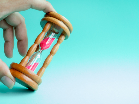 Hand Holding The Wooden Vintage Hourglass with Pink Sand on Blue Background, Sand Running through the Bulbs for Measuring The Passing Time in A Countdown to Deadline.の写真素材
