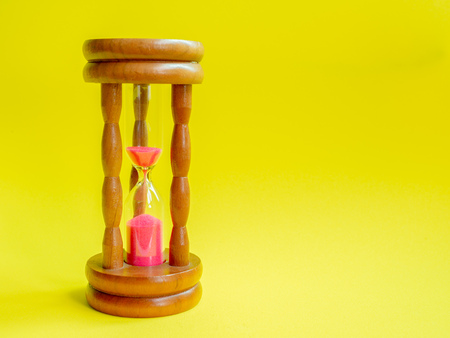 Wooden Vintage Hourglass with Pink Sand on Yellow Background, Sand Running through the Bulbs for Measuring The Passing Time in A Countdown to Deadline.の写真素材