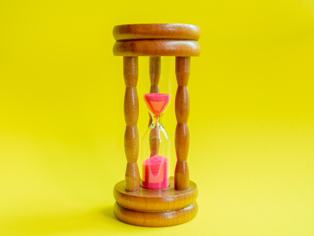 Wooden Vintage Hourglass with Pink Sand on Yellow Background, Sand Running through the Bulbs for Measuring The Passing Time in A Countdown to Deadline.の写真素材