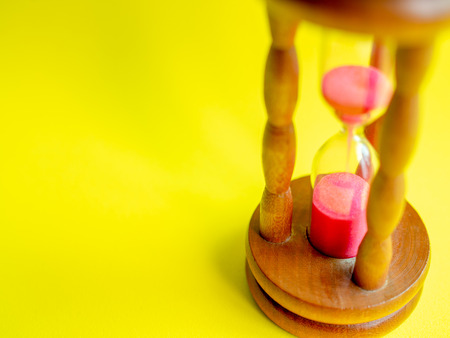 Close-up Wooden Vintage Hourglass with Pink Sand on Yellow Background, Sand Running through the Bulbs for Measuring The Passing Time in A Countdown to Deadline.の写真素材