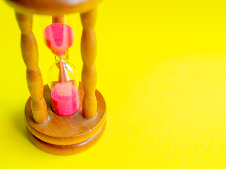 Close-up Wooden Vintage Hourglass with Pink Sand on Yellow Background, Sand Running through the Bulbs for Measuring The Passing Time in A Countdown to Deadline.の写真素材