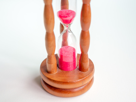 Close-up Wooden Vintage Hourglass with Pink Sand on White Background, Sand Running through the Bulbs for Measuring The Passing Time in A Countdown to Deadline.の写真素材
