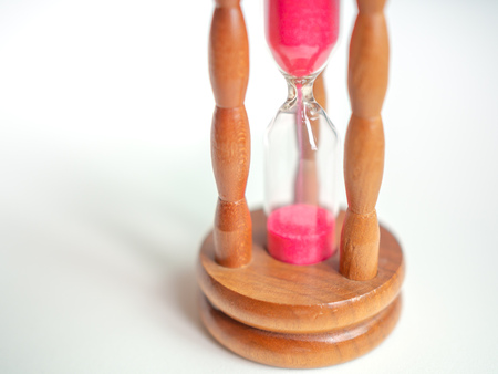 Close-up Wooden Vintage Hourglass with Pink Sand on White Background, Sand Running through the Bulbs for Measuring The Passing Time in A Countdown to Deadline.の写真素材