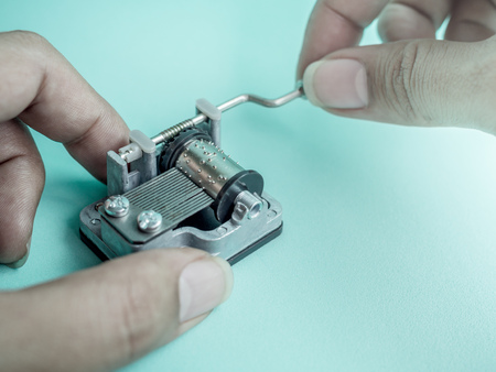 Hands Playing Vintage Small Mechanical Music Box Isolate on Blue Backgroundの写真素材