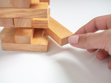 Hand Move out The Block Playing Tumble Tower Wooden Block Game on White Background. Business Conceptの写真素材