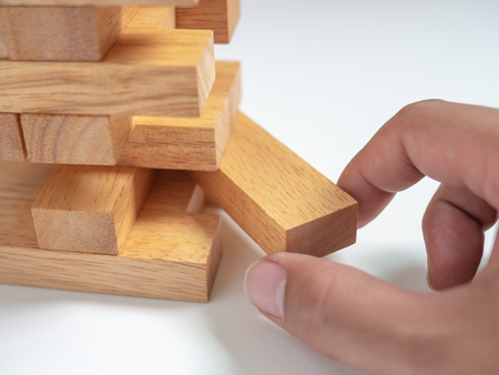 Hand Move out The Block Playing Tumble Tower Wooden Block Game on White Background. Business Conceptの写真素材