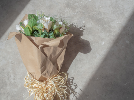 Artificial White Roses Bouquet in Wrapping Brown Craft Paper in The Light Between The Shadow on Concrete Backgroundの写真素材