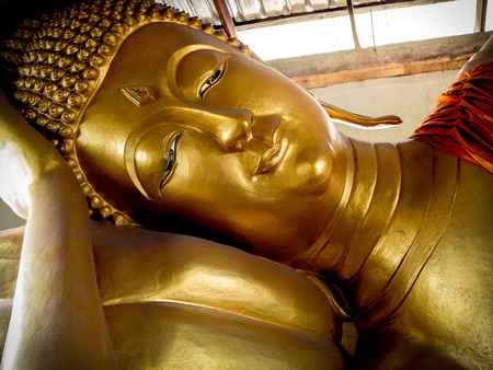 Reclining Golden Buddha Statue. Close-up Beautiful Sleeping Buddha Face under The Roof of Local Temple in Thailandの写真素材