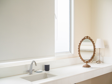Clean White Bathroom Interior with Sink Basin Faucet, Vintage Mirror, White Lamp, Soap and Ceramic Mug Near The Glass Window. Modern Design of Bathroom with Copy Space.の写真素材