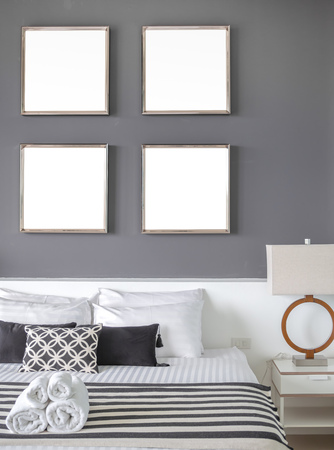 Modern Bedroom with Four Square Blank Stainless Steel Frames on The Gray Wall Interior, Pillows and Towels on The Bed with Side Lamp.の写真素材