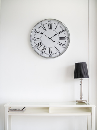 White Modern Book Table with Black Lamp and Vintage Round Clock on Clean White Wall Background with Copy Space.の写真素材