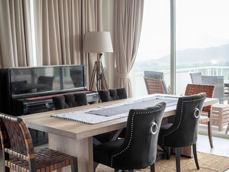 Modern Luxury Dining Room Interior with Wooden Dining Table, Luxury Chairs on The Carpet, Classic Piano, Floor Lamp and The Curtain Near The Terrace Outside with Mountain View.の写真素材