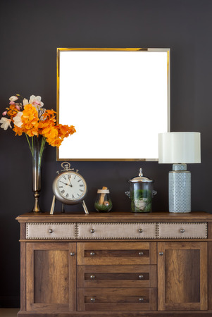 Vintage Interior of Living Room, Vintage Clock, Flowers in Vase, Plant and Roll of Paper in Bottle and Ceramic Porcelain
Lamp on Wooden Cabinet and Blank Luxury Golden Frame Mock-up on Black Wall.の写真素材