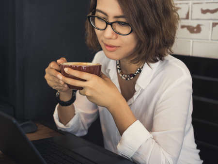 Beautiful Asian Woman wearing glasses and white shirt drinking coffee and watching to her black...