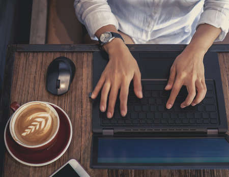 Hand typing on Black laptop computer with computer mouse, concentrated at working with coffee and...