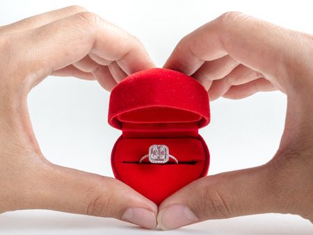 Diamond ring in red heart shape box in hart shape hands isolated on white background.の写真素材