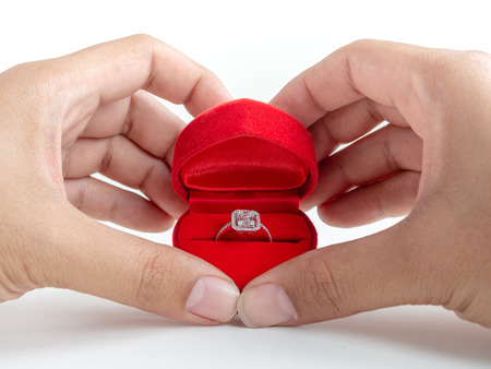 Diamond ring in red heart shape box in hands isolated on white background.の写真素材