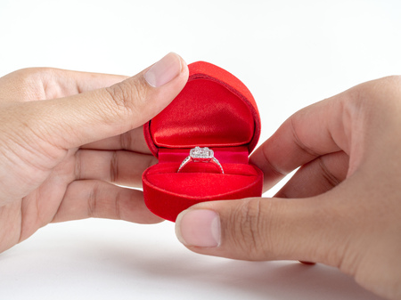 Diamond ring in red heart shape box in hands isolated on white background.の写真素材