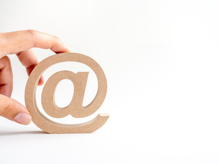 Hand putting wooden E-mail address symbol, arroba icon isolated on white background with copy space. E-mail marketing online internet concept.の写真素材
