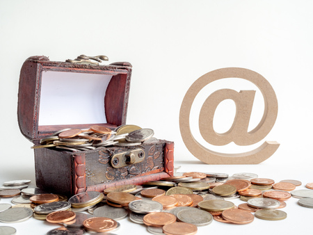 Money coins stack with treasure chest and wooden email address symbol or arroba icon isolated on white background. E-mail marketing online and financial concept.の写真素材