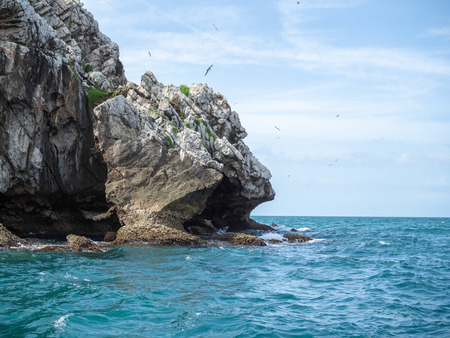 The corner of the rock cliff island mountain in the sea with the birds flying in the sky on sunny day.の写真素材