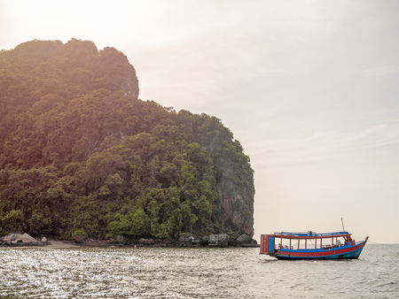 Wooden local travel passenger ferry boat on the sea near the rock mountain on blue sky background with sunlight in Thailand.の写真素材