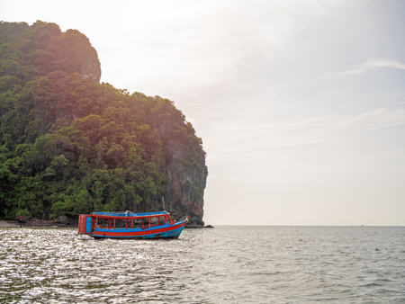 Wooden local travel passenger ferry boat on the sea near the rock mountain on blue sky background with sunlight in Thailand.の写真素材