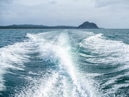 Water stream from the fast moving of the motor boat on the sea with island view in rainy day. Travel destination in Thailand.の写真素材