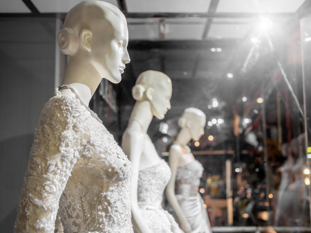 White female mannequin in wedding dress in showcase. Bridal dresses on the mannequins in wedding window display with light on wedding suit shop background.の写真素材