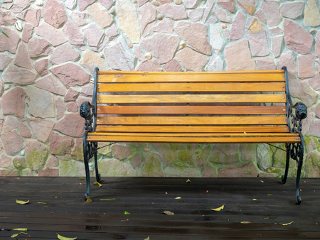 Long wooden chair and leaves on wooden wet floor after rain on stone wall background.の写真素材