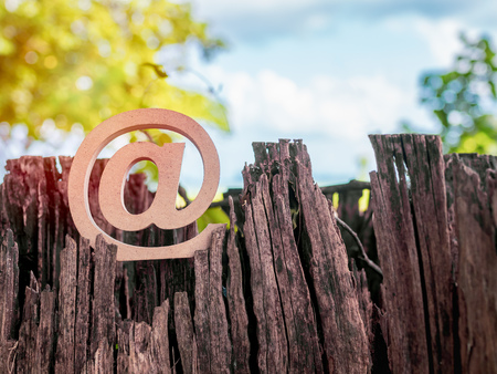 Wooden E-mail address symbol, arroba icon on dry stump on green tree and blue sky background with sunlight. E-mail marketing online internet, technology and environment concept.の写真素材