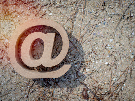 Wooden E-mail address symbol, arroba icon on sand beach texture background with sunlight with copy space. E-mail marketing online internet, technology and environment concept.の写真素材