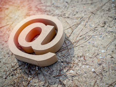 Wooden E-mail address symbol, arroba icon on sand beach texture background with sunlight with copy space. E-mail marketing online internet, technology and environment concept.の写真素材