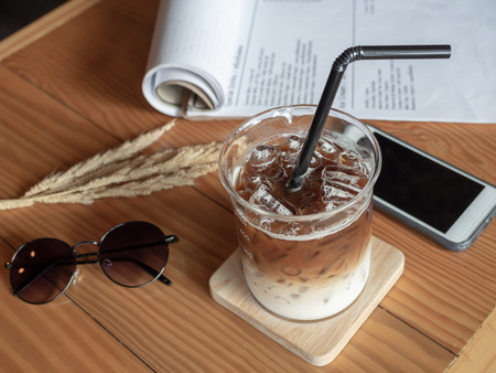 Ice coffee in beaker cup with black tube, mobile phone, sunglasses and paper on wooden table in vintage style cafe. coffee unique concept.の写真素材