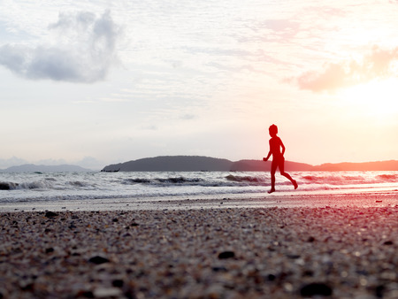Silhouette of the little girl running on the beach with sunlight on sunset.の写真素材